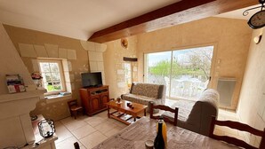 Ein Wohnzimmer mit einer Couch, einem Fernseher, einem Holzkabinett und einem Tisch mit einer Flasche und einem Korb.