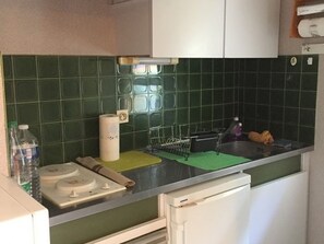 A kitchen with green tiles, a roll of paper towels, a water bottle, and a dish rack. - Cozy apartment with AC - 4 guests, near the beach (Argelès-sur-Mer)