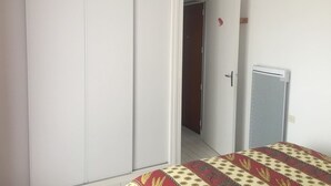 Une chambre avec une armoire, un lit recouvert d’une couvre-lit à motifs et un petit radiateur fixé au mur.
