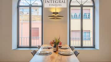 A dining area with a wooden table set for four, two large windows with balconies, and a sign reading 'INTEGRAL FINQUES'.