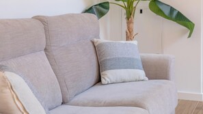 A beige sofa with two pillows, a potted plant, and a white wall. - Bright apartment with air conditioning - 2 guests (Palamós)