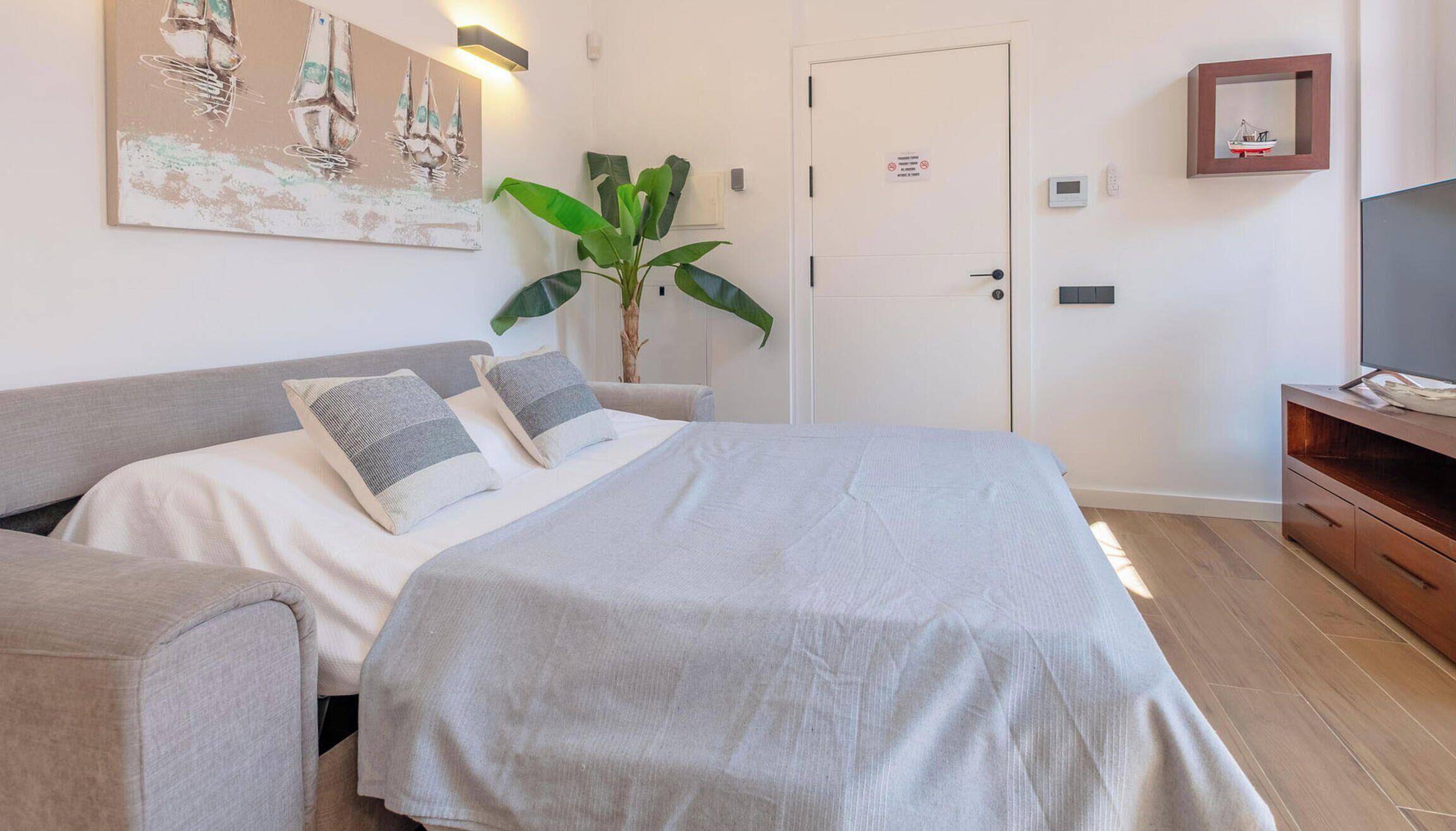 A bedroom with a bed, bedside tables, a plant, a door with a sign, and a TV on a wooden cabinet.