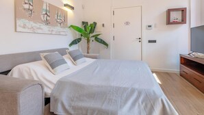 Un dormitorio con una cama, mesitas de noche, una planta, una puerta con un cartel y un televisor sobre un mueble de madera.