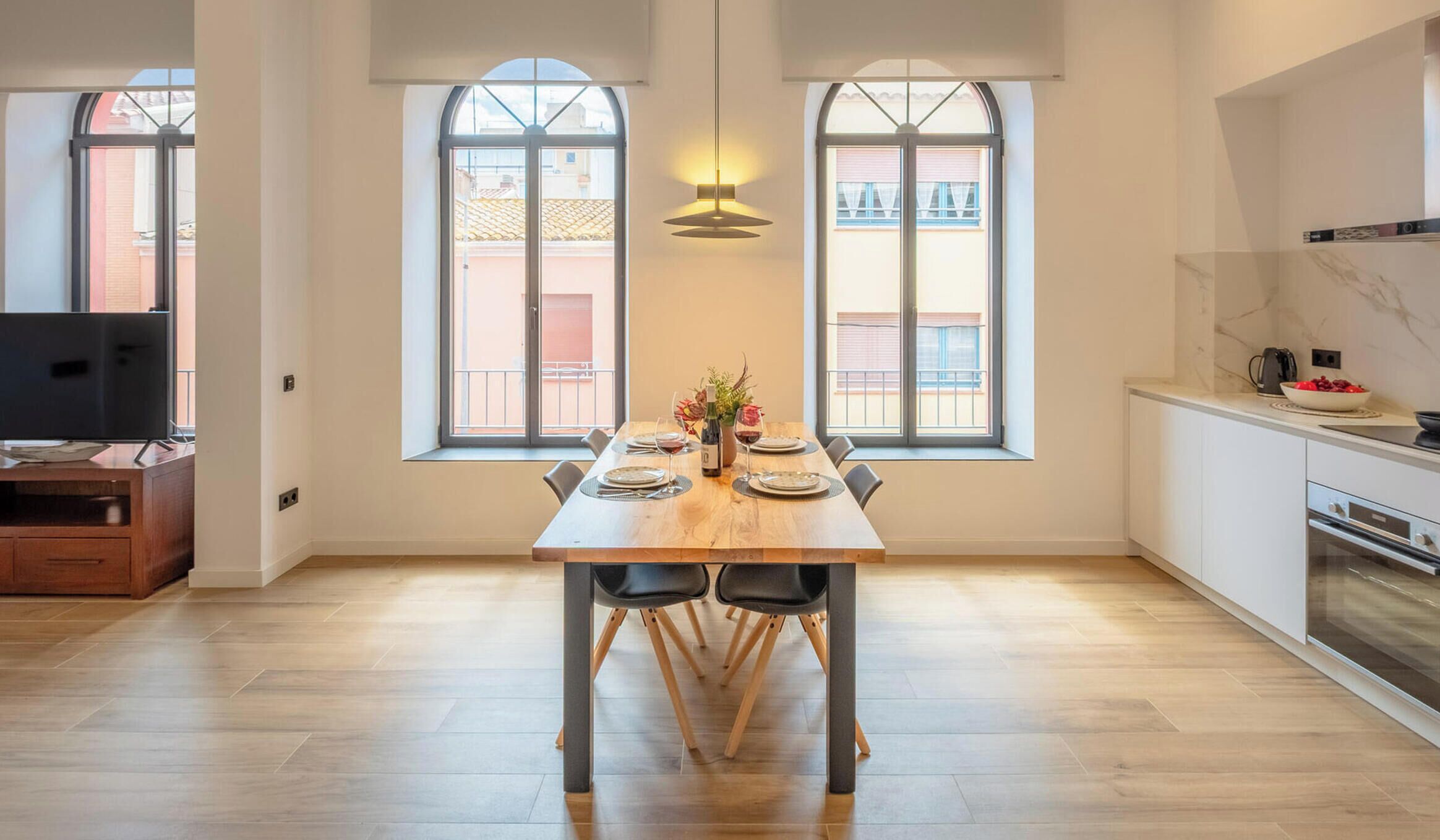 A modern kitchen with a dining area, large windows, and a TV.