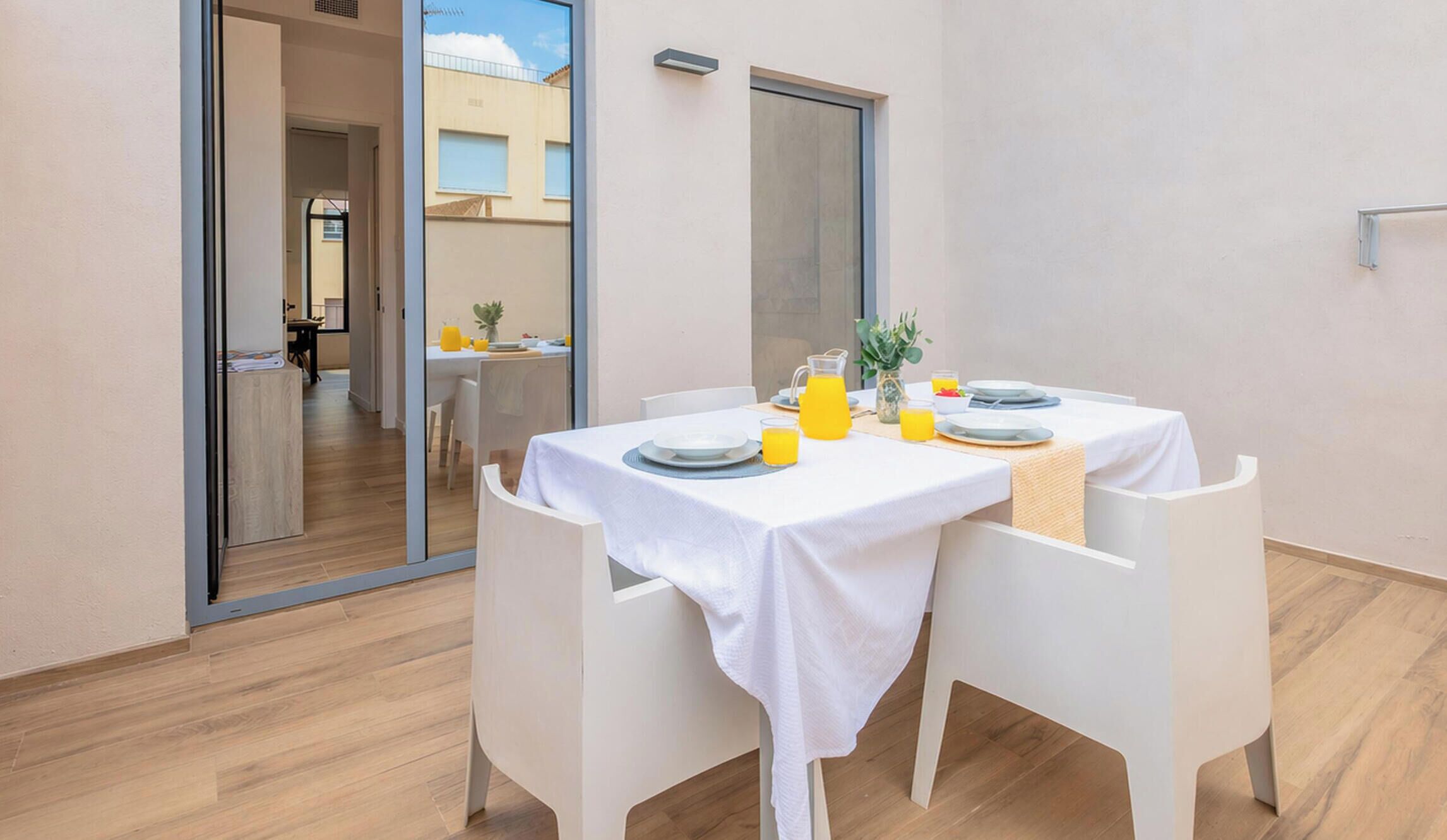 A dining area with a table set for two, a small plant, and a glass of orange juice.