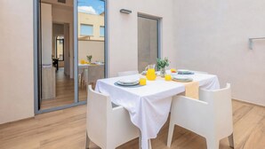 Un área de comedor con una mesa dispuesta para dos personas, una planta pequeña y un vaso de zumo de naranja.