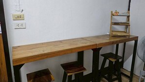 A wooden desk with a shelf, two stools, and a fan.