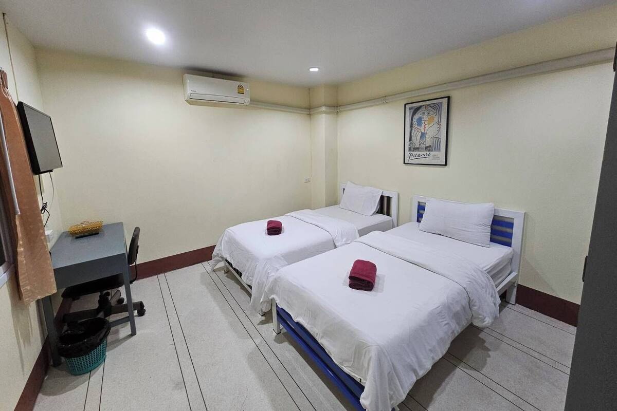 A hotel room with two beds, a desk, a chair, a TV, an air conditioner, and a framed picture on the wall.