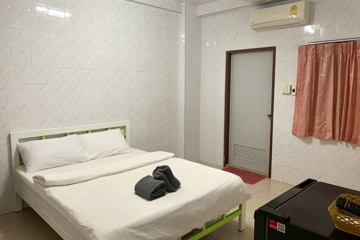 A hotel room with a bed, a desk, an air conditioning unit, and a door.