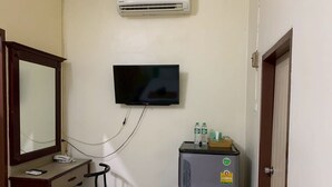 A small room with a desk, chair, mirror, television, and a refrigerator.
