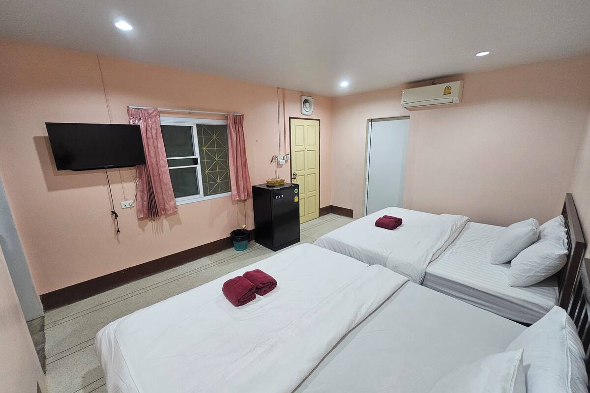 A hotel room with two beds, a TV, a wardrobe, and an air conditioning unit.