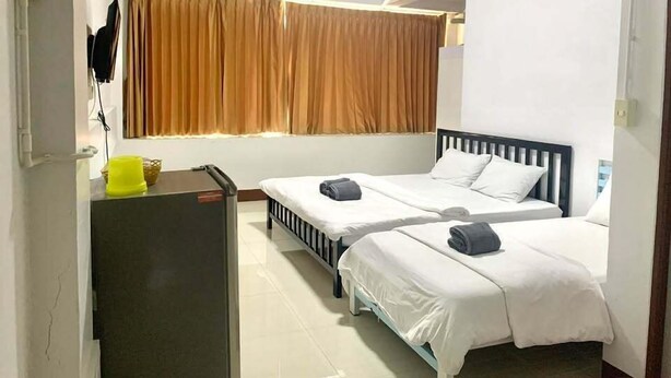 A hotel room with two beds, a desk, a chair, a small table, a window with curtains, and an air conditioning unit.