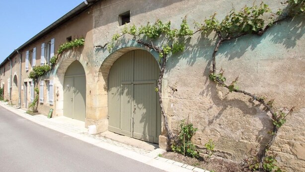 A row of stone buildings with arched doorways, a paved street, and some greenery growing on the walls. - Cozy group cottage in Bucey-lès-Gy, perfect for hikers (Bucey-lès-Gy)