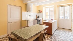 A compact kitchen with white cabinets, a central island, and a dining area with a table and chairs. - Cozy group cottage in Bucey-lès-Gy, perfect for hikers (Bucey-lès-Gy)