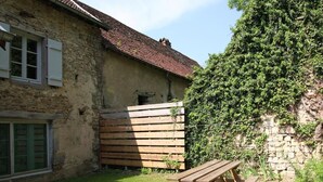 A stone building with a wooden fence, a wooden table, and a grassy yard. - Cozy group cottage in Bucey-lès-Gy, perfect for hikers (Bucey-lès-Gy)