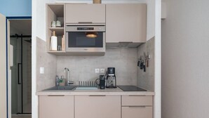 Una cocina compacta con microondas integrado, cafetera y lavamanos.