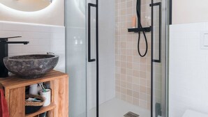 Un baño moderno con cabina de ducha de vidrio, tocador de madera con lavabo y un espejo redondo.
