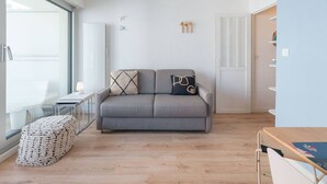 Una sala moderna con un sofá gris, una mesita auxiliar y un reposapiés tejido.