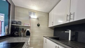 Eine moderne Küche mit weißen Schränken, einer schwarzen Arbeitsplatte, einer Kaffeemaschine und einem kleinen Regal mit beschrifteten Behältern.