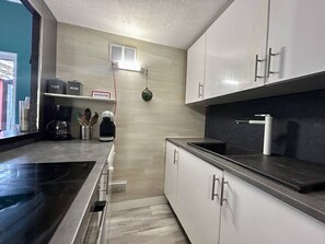 Una cocina moderna con armarios blancos, una encimera negra, una cafetera y un estante pequeño con recipientes etiquetados.