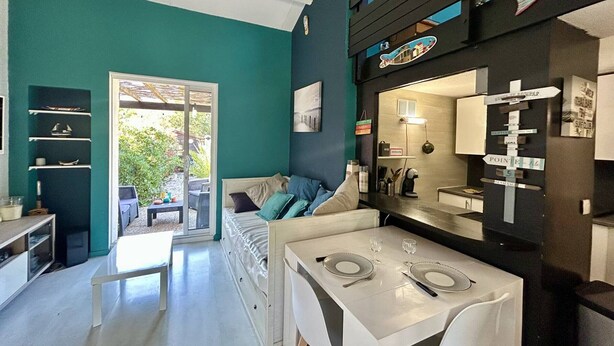Ein modernes Interieur mit einer Türkiswand, einem Essbereich mit einem weiß gedeckten Tisch, einer Couch mit Kissen und einer schwarzen Wand mit einem Schild.