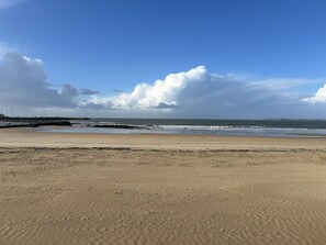 Ein Strand mit felsigem Ufer, blauem Himmel und Gebäuden in der Ferne.