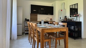 Et moderne køkken med sorte skabe, et hvidt køleskab og et spiseområde med træstole og et bord dækket til fire personer.