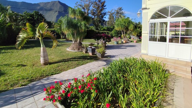 A pathway leading to a building with a garden and a mountain in the background.