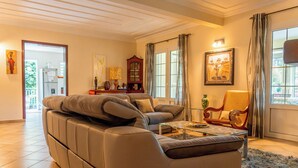 A living room with a sofa, armchair, and a glass coffee table. There is a wooden cabinet and a painting on the wall.