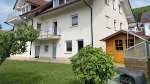A two-story residential building with a balcony, a wooden structure attached to the right side, and a well-maintained lawn. - Vacation apartment Loder 108 m2 (Blumberg)
