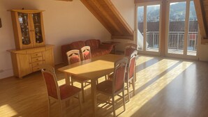 A dining area with a wooden table and chairs, a cabinet with glass doors, and a view of a residential area through large windows. - Vacation apartment Loder 108 m2 (Blumberg)
