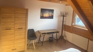 A bedroom with a wooden wardrobe, a desk, a chair, a coat rack, a radiator, and a window with a view. - Vacation apartment Loder 108 m2 (Blumberg)