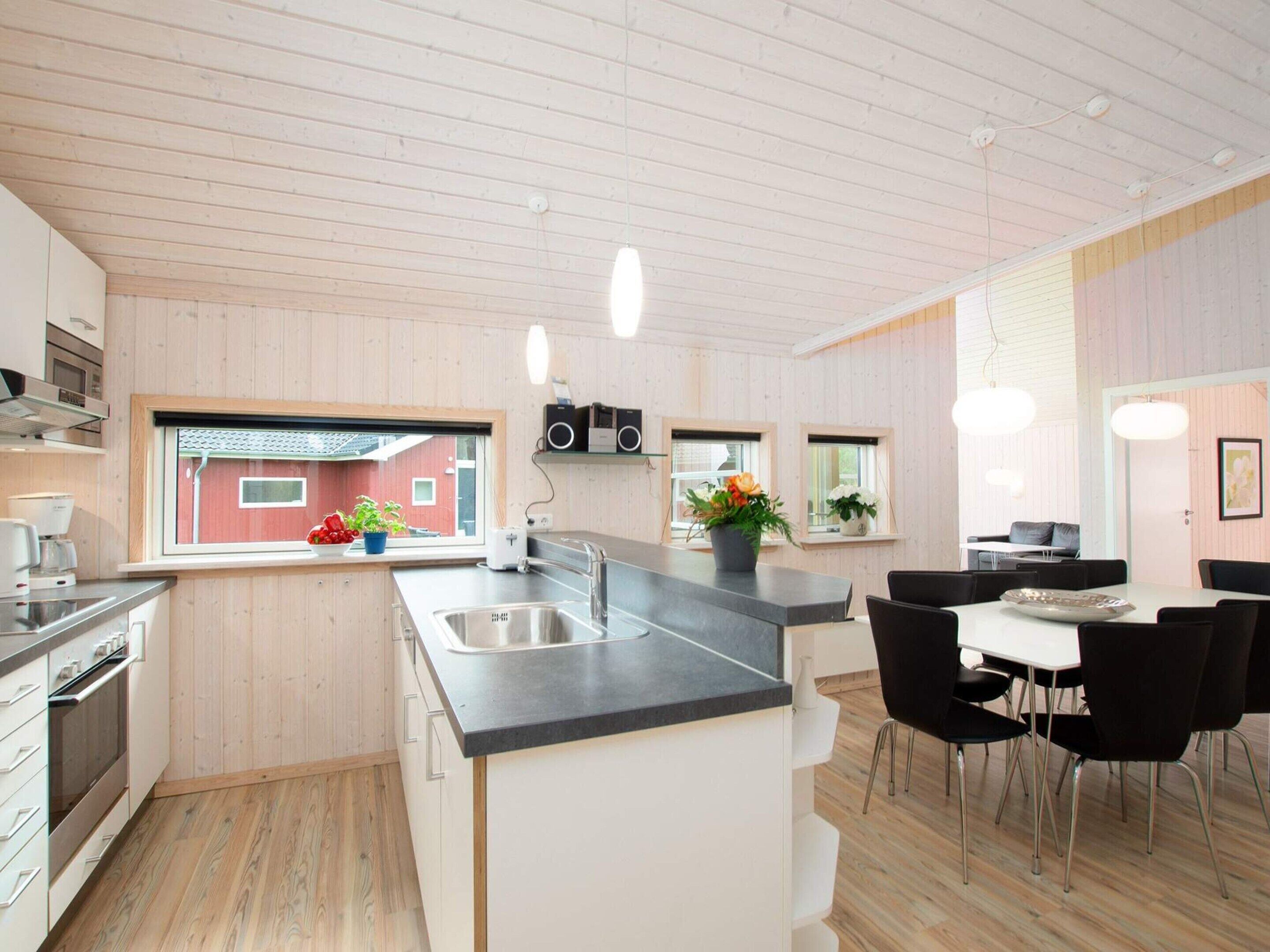 Et moderne køkken med en central ø, integrerede hårde hvidevarer og et spiseområde med bord og stole.