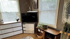 A living room with a flat-screen TV, a wooden bench, a large rug, and a potted plant.