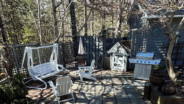 A deck with a grill, chairs, and a small shed.