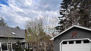 A residential garage with a 'Guest Parking' sign, a gravel driveway, and a house with a chimney and a star decoration on the garage.
