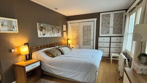 A bedroom with a bed, bedside tables, a nightstand, a dresser, a chair, and a window with curtains.