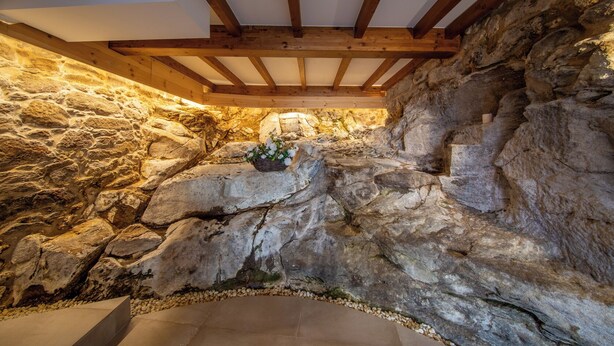 Ein Steininterieur mit Holzbalken, einer Steinwand und einem kleinen Korb mit Blumen.