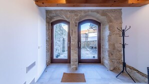 Ein Zimmer mit steinernen Bögen, Holzbalken, einem Garderobeständer und Blick auf einen Innenhof.