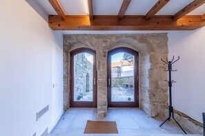 Ein Zimmer mit steinernen Bögen, Holzbalken, einem Garderobeständer und Blick auf einen Innenhof.