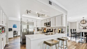 Cozinha moderna com armários brancos, eletrodomésticos de aço inoxidável e uma ilha central com banquetas.