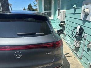 Ein grauer Mercedes-Benz 4MATIC steht neben einem grünen Gebäude mit einer Ladestation.
