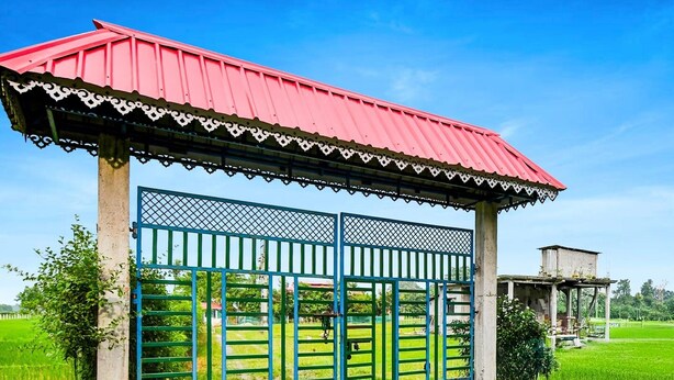 Una estructura con techo rojo y puertas azules, rodeada de campos verdes.