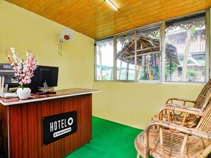 A hotel reception desk with a 'HOTEL' sign, a computer, a fan, and a wicker chair. - Classic With Balconymoner Manush (Alipurduar)