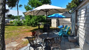 An outdoor patio with a table and chairs, a barbecue grill, and a covered seating area. - Escape to this charming 1-bedroom Cape cottage, .4 miles to the beach (Dennis Port)