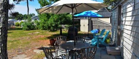 An outdoor patio with a table and chairs, a barbecue grill, and a covered seating area.