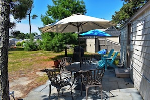 Eine Terrasse im Freien mit Tisch und Stühlen, einem Grill und einer überdachten Sitzgruppe.