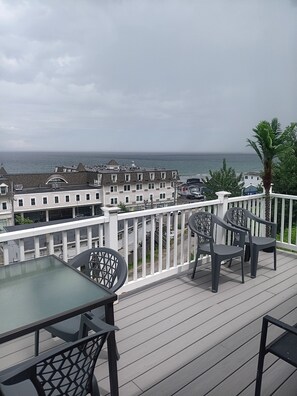 A balcony with a table and chairs, overlooking a residential area and the ocean.