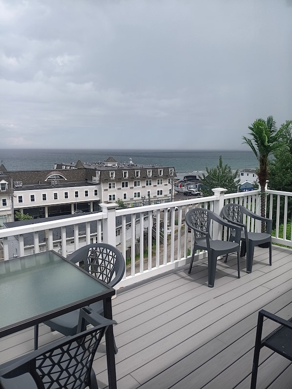 A balcony with a table and chairs, overlooking a residential area and the ocean. - DIRECT OCEAN VIEWS 36 FT DECK Spacious 4-bedroom condo in superb Hull with AC (Hull)