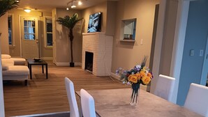 Un área de comedor con una mesa y sillas, una chimenea y una sala de estar al fondo.